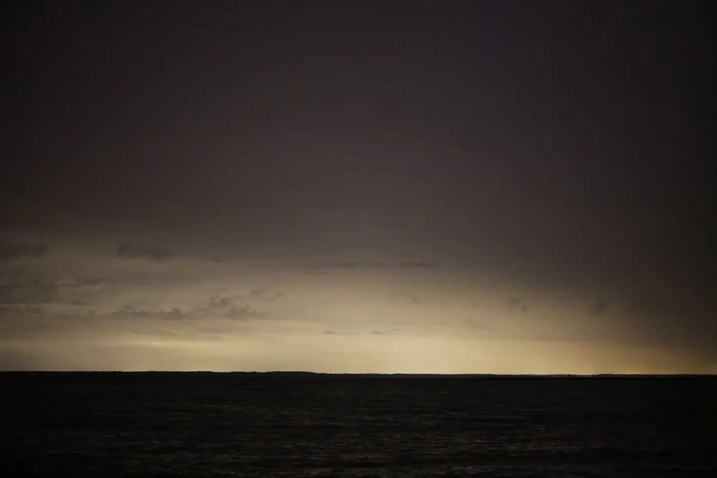 A dark, moody ocean horizon at dusk, with the last light fading under a cloudy sky.